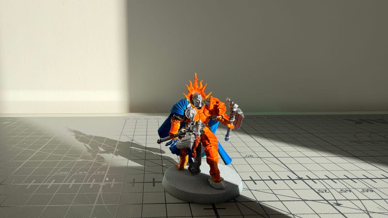The finished Reclusian in bright sunlight on a cutting mat, its orange armour and blue cloak casting a long shadow.